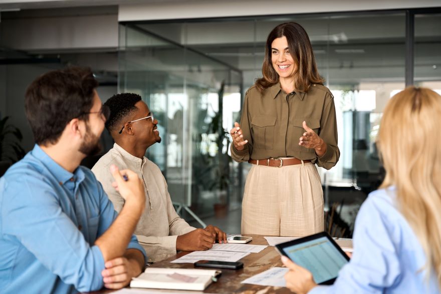 A woman manager happily talking to work team that is sat around a desk