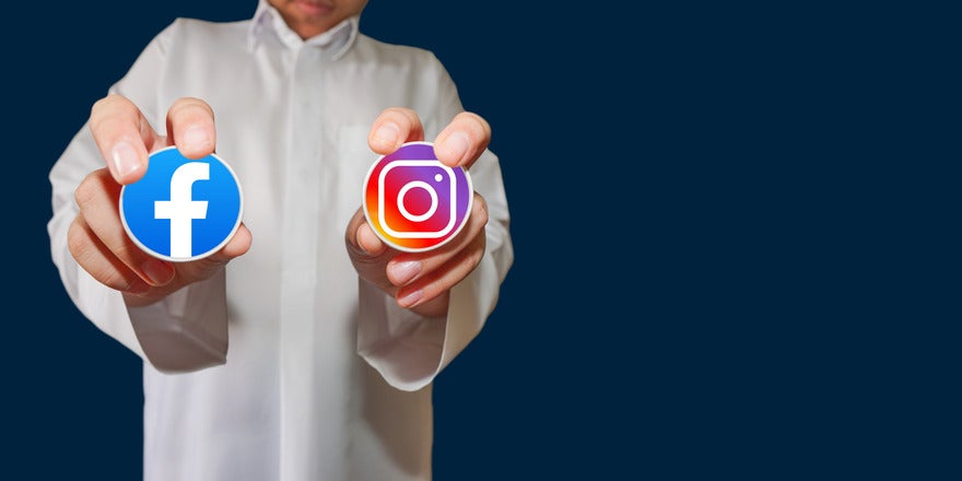 Person in white shirt holding up a sticker of the Facebook logo and the Instagram logo in each hand