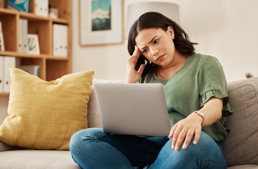 Woman looking puzzled with her hand against her head as she stares at a laptop