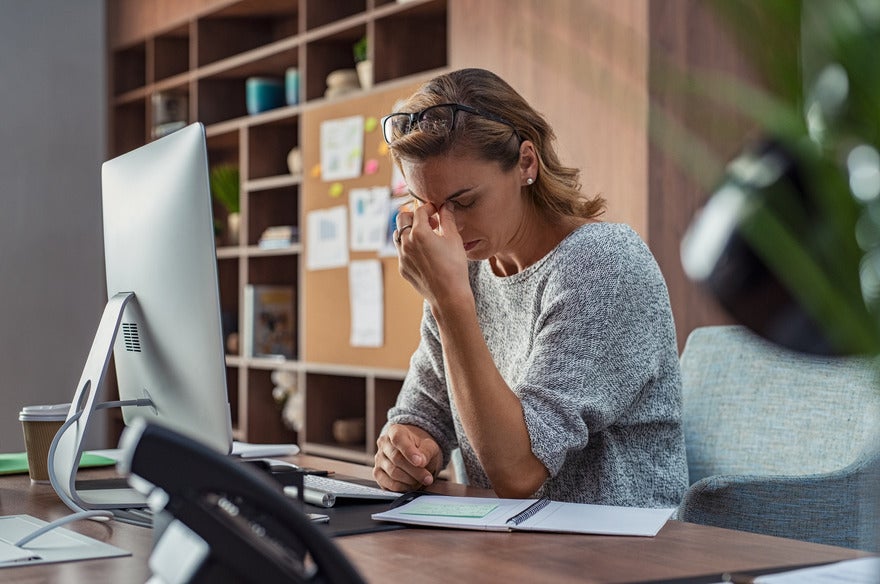 Woman holding her head in front of a desktop computer