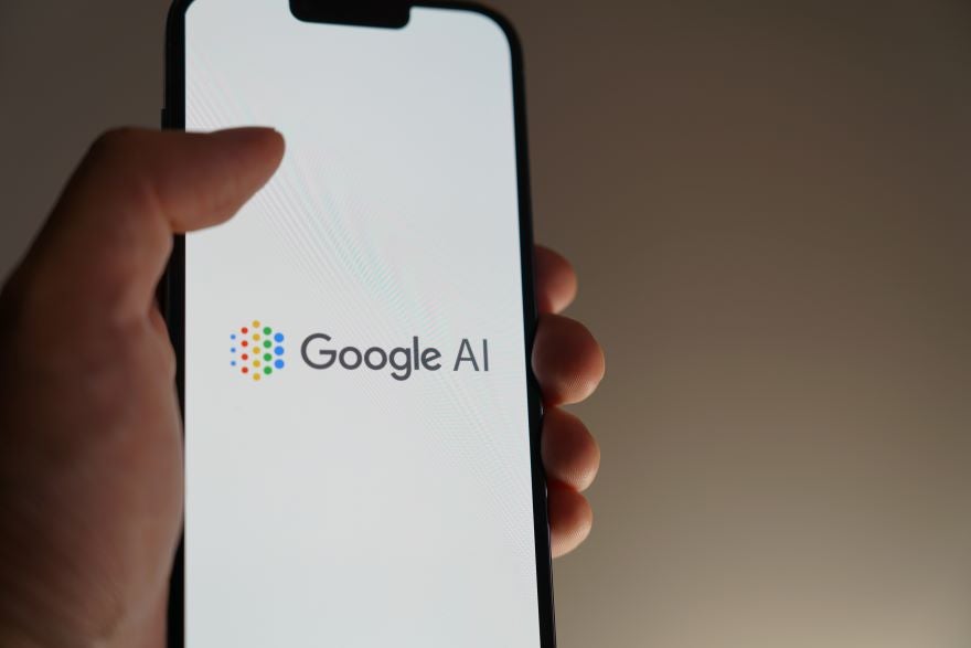 A hand holding a phone with the "Google AI" logo on screen