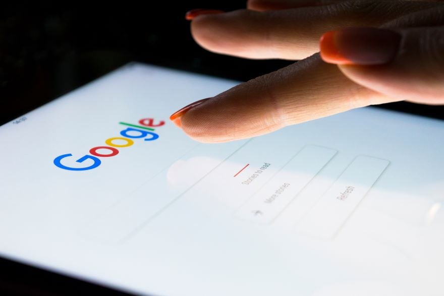 Closeup of a hand tapping a smartphone screen on the Google homepage