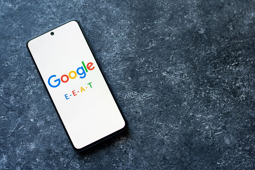 A phone with the google logo on the screen and text reading "E-E-A-T"
