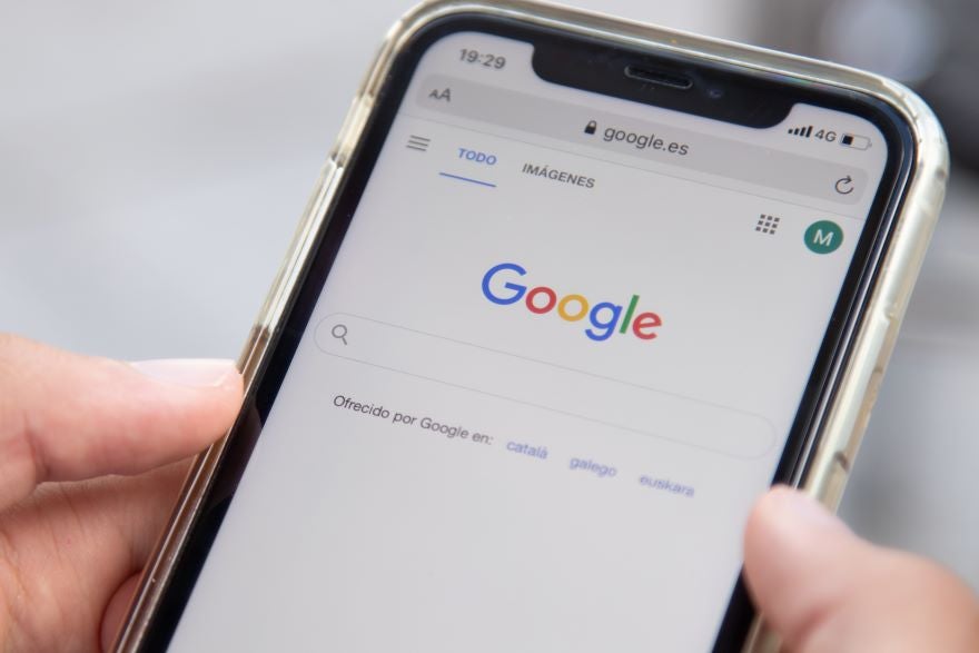 A hand holding a phone with Google search on screen