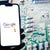 A hand holds a smartphone displaying the Google Reviews logo against a blurred circuit board background.