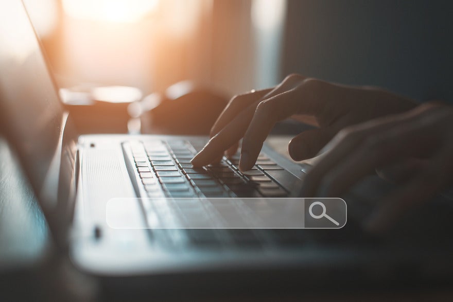 Hands typing at a laptop with a floating image of a search bar on top