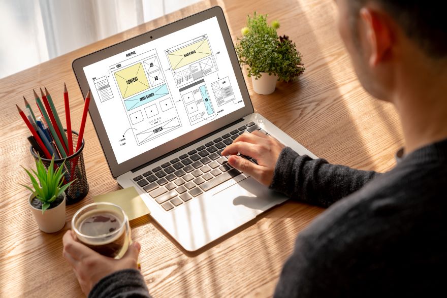 A man using his laptop with a homepage wireframe on the screen