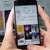 Hands hold a mobile phone showing Instagram's profile on Instagram, with a desktop behind also showing the same image