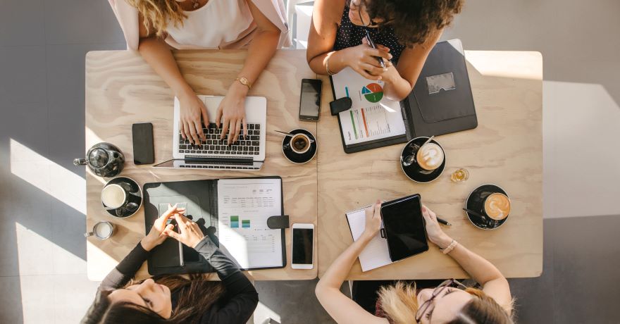 Women sat at a desk talking with their work on the table.