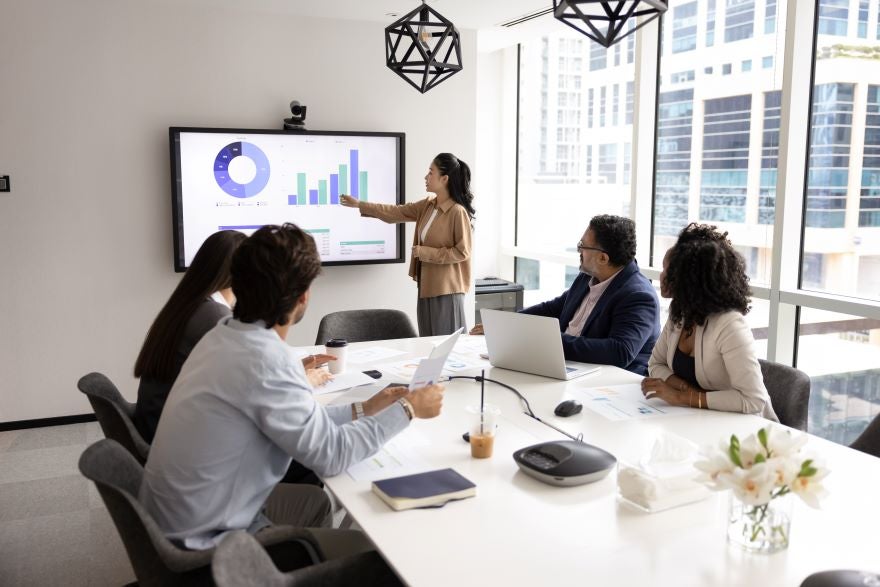 Colleagues sitting around a table watching a manager present on screen