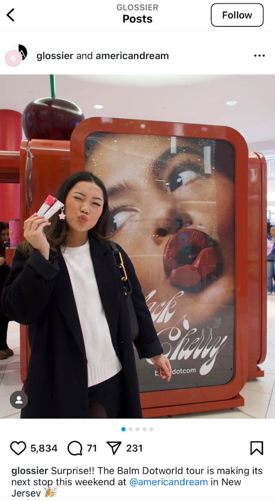 Woman stood next to makeup ad holding lipstick and pouting