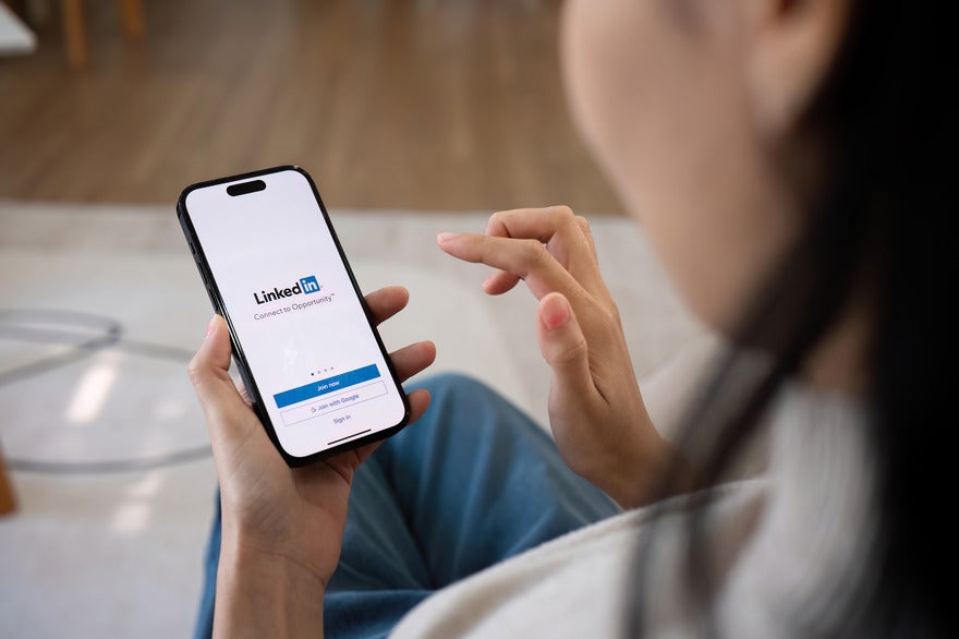 Woman holding a mobile phone with the LinkedIn login page on screen