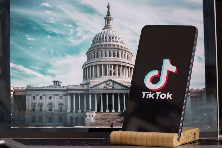 A phone with the TikTok logo on screen in front of a photo of the White House