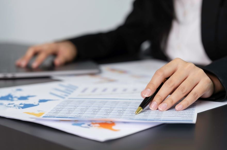A closeup of paperwork on a desk and someone's hands pointing at a sheet with a pen in hand