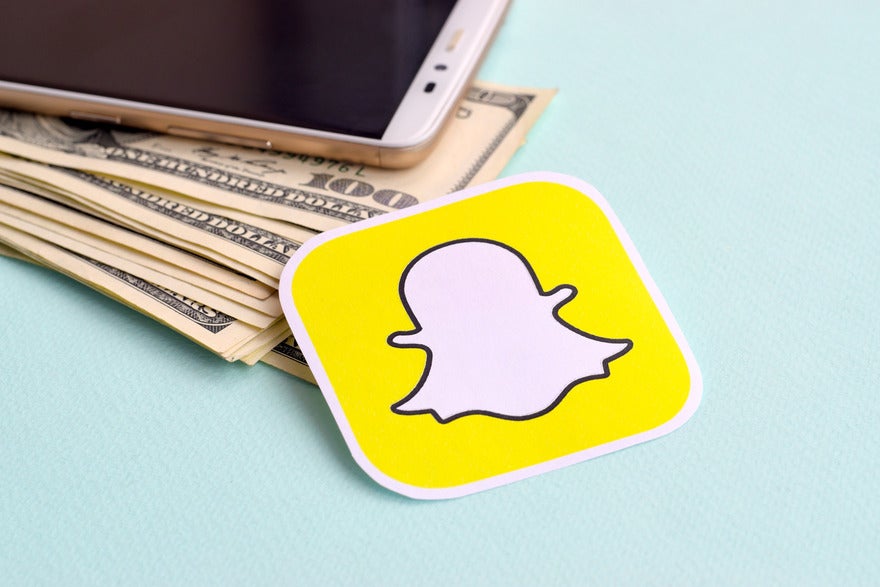 Sticker of snapchat logo laying on top of pile of dollar notes