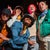 A group of five people in colorful streetwear poses playfully at night, with a vibrant pink light illuminating the background.