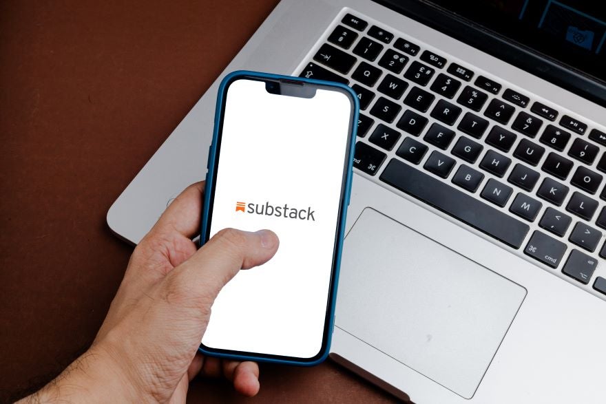A hand using a smartphone with the Substack logo on screen