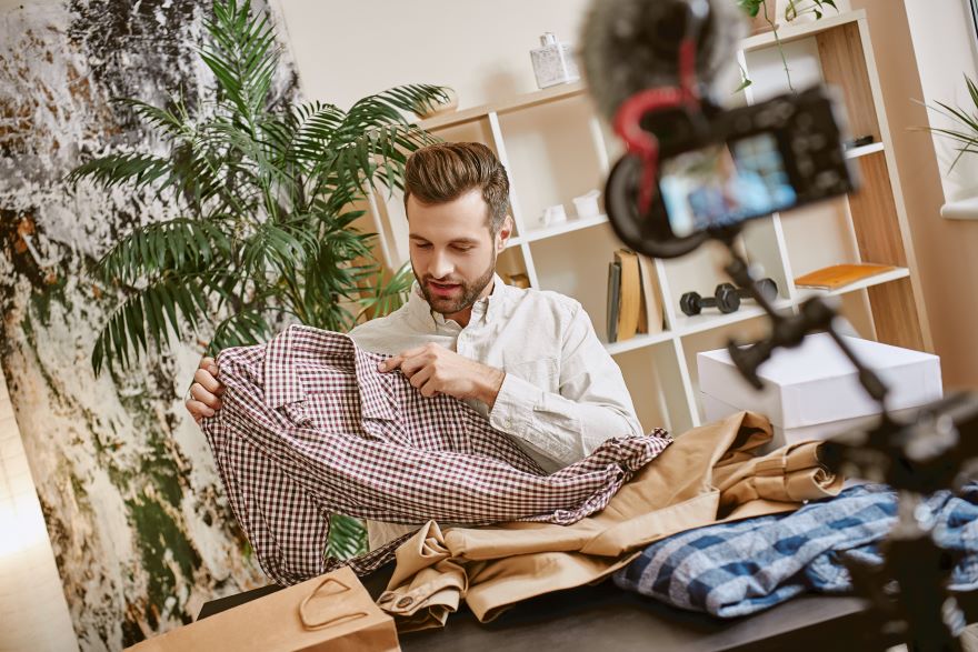 Screenshot of a man showcasing a shirt in front of a camera on a tripod
