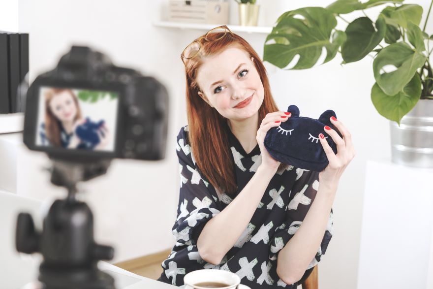 A smiling woman holding a bag in front of a video camera on record